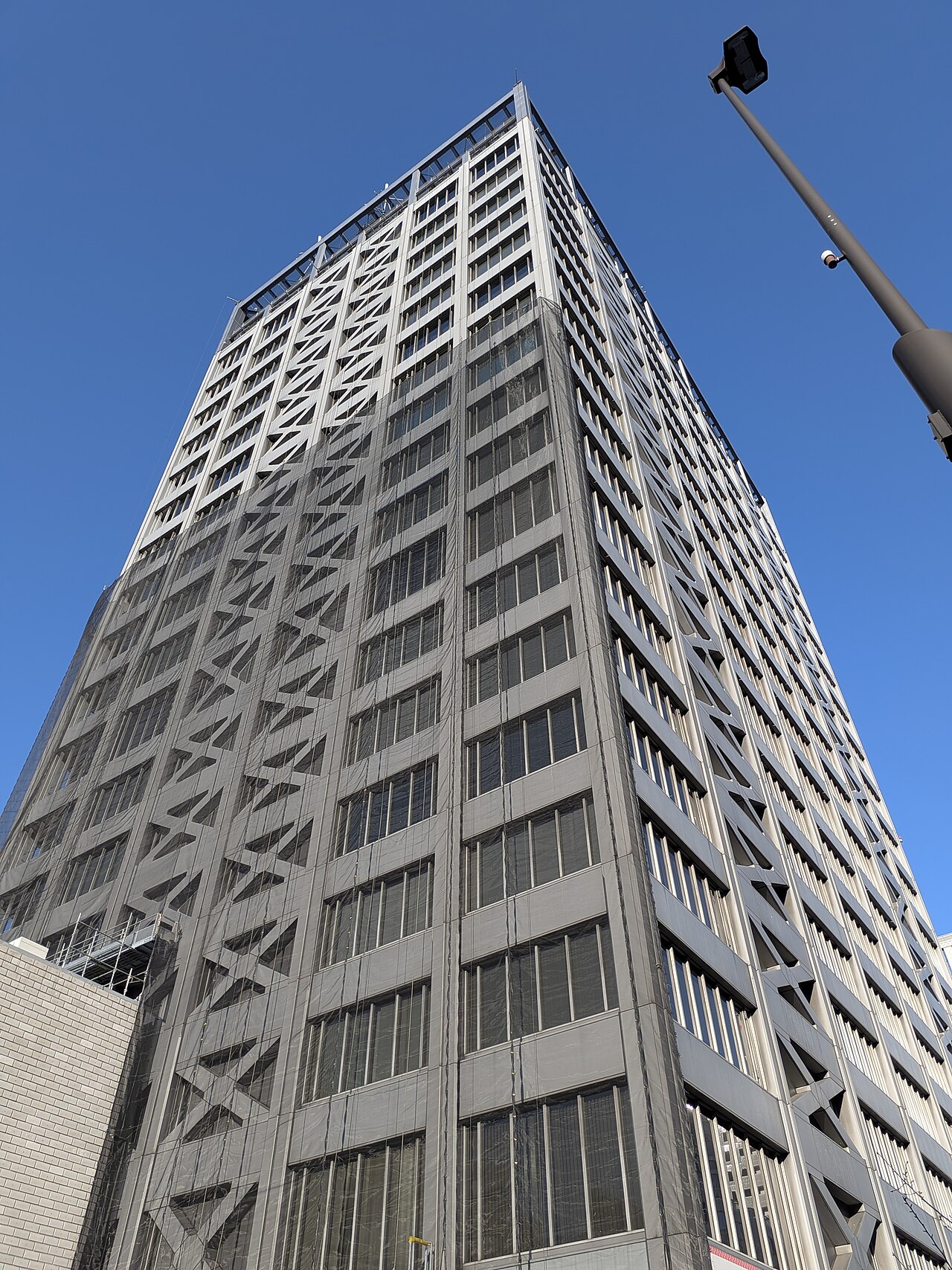 Edificio alto de oficinas con fachada de concreto y ventanas rectangulares, visto desde abajo contra un cielo azul despejado. Fotografía de archivo.
