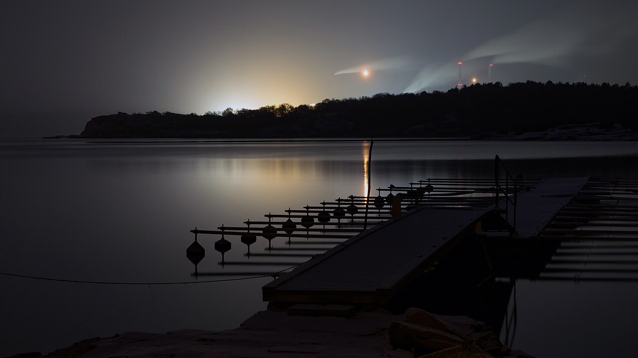 Refinería iluminada al otro lado de Brofjorden, Suecia, durante una nevada nocturna.